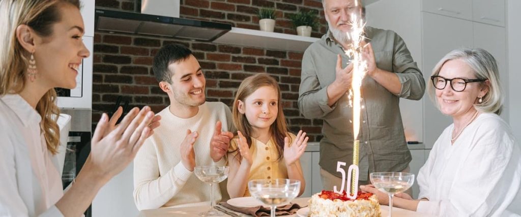 femme fêtant ses 50 ans, avec sa famille, avec une bougie à étincelles sur le gâteau.