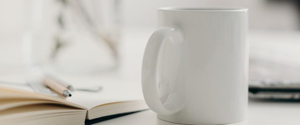 mug blanc posé à côté d'un livre et d'un stylo